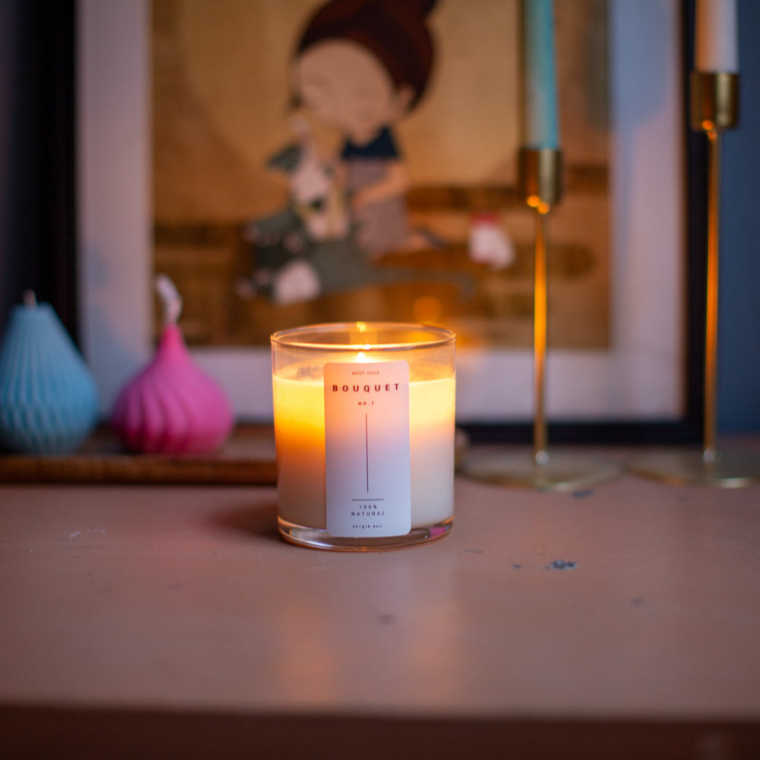Lit Bouquet candle by Meet Haus on a wooden surface with decor and artwork in the background.