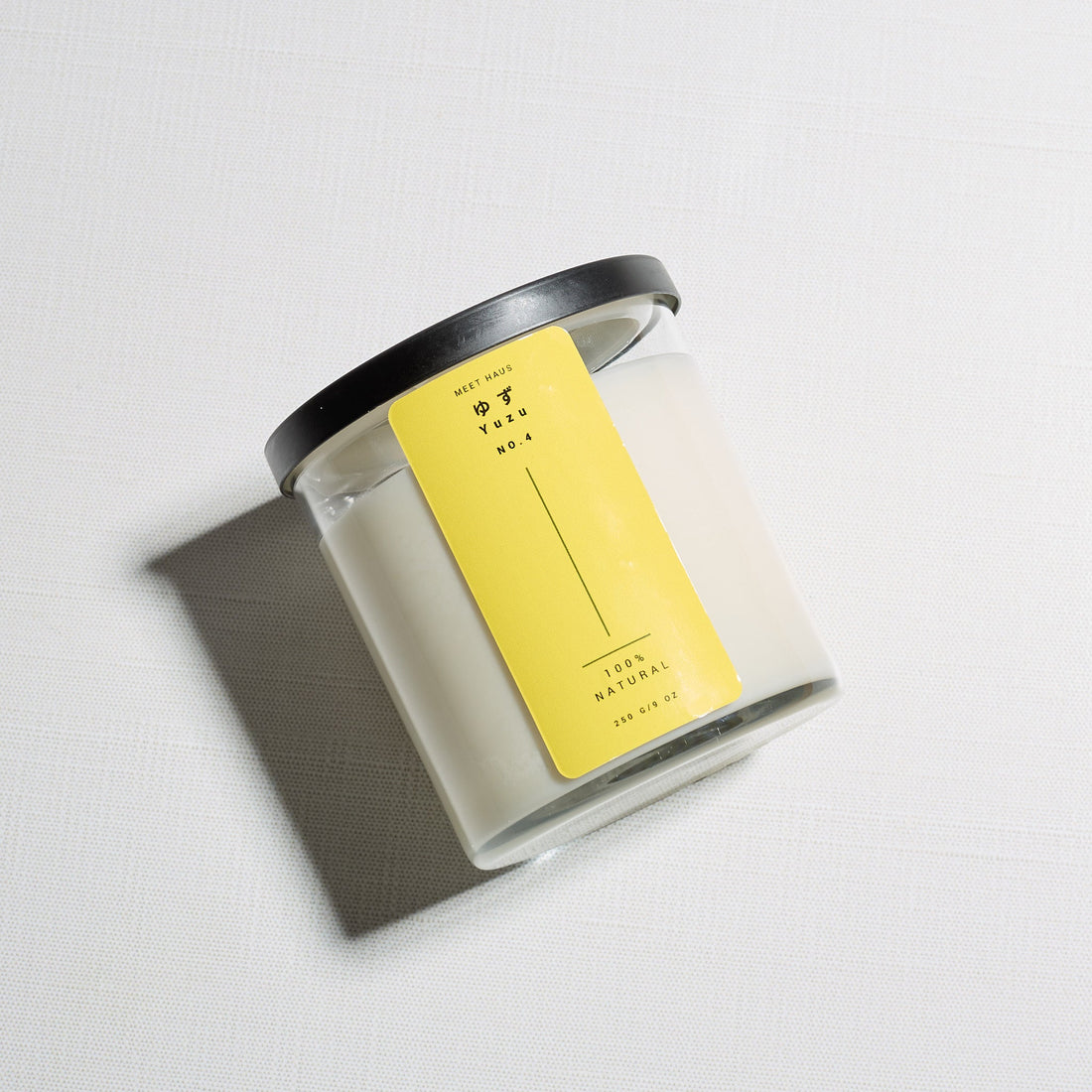 Yuzu candle on its side with the label up on a light linen background. 