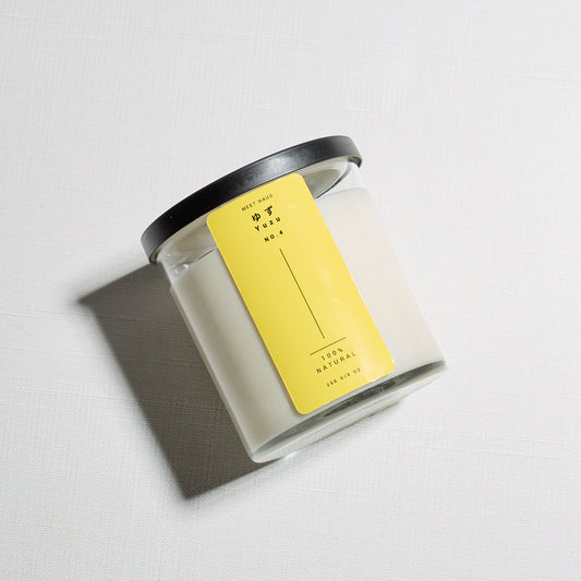 Yuzu candle on its side with the label up on a light linen background. 
