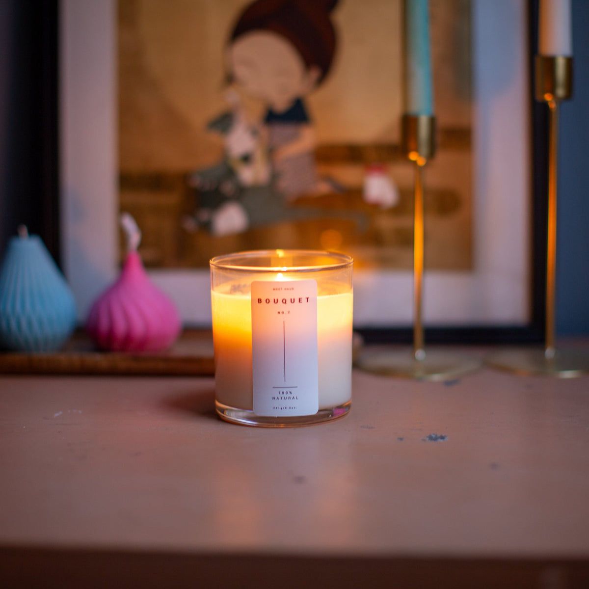 Lit Bouquet candle by Meet Haus on a wooden surface with decor and artwork in the background.