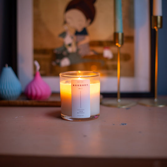 Lit Bouquet candle by Meet Haus on a wooden surface with decor and artwork in the background.