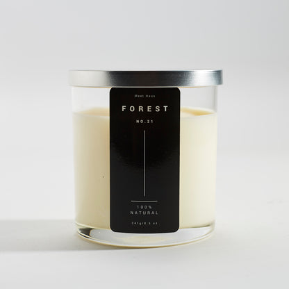 An unlit Meet Haus Forest No. 21 natural soy candle without the lid, revealing the creamy white wax, displayed on a concrete background with the black and white label facing forward.