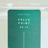 Meet Haus Fells Point soy candle, a Baltimore neighborhood scent: close-up of the green jar label, Meet Haus, Fells Point, No. 14, in white type with a thin line, seen through clear glass over white wax.